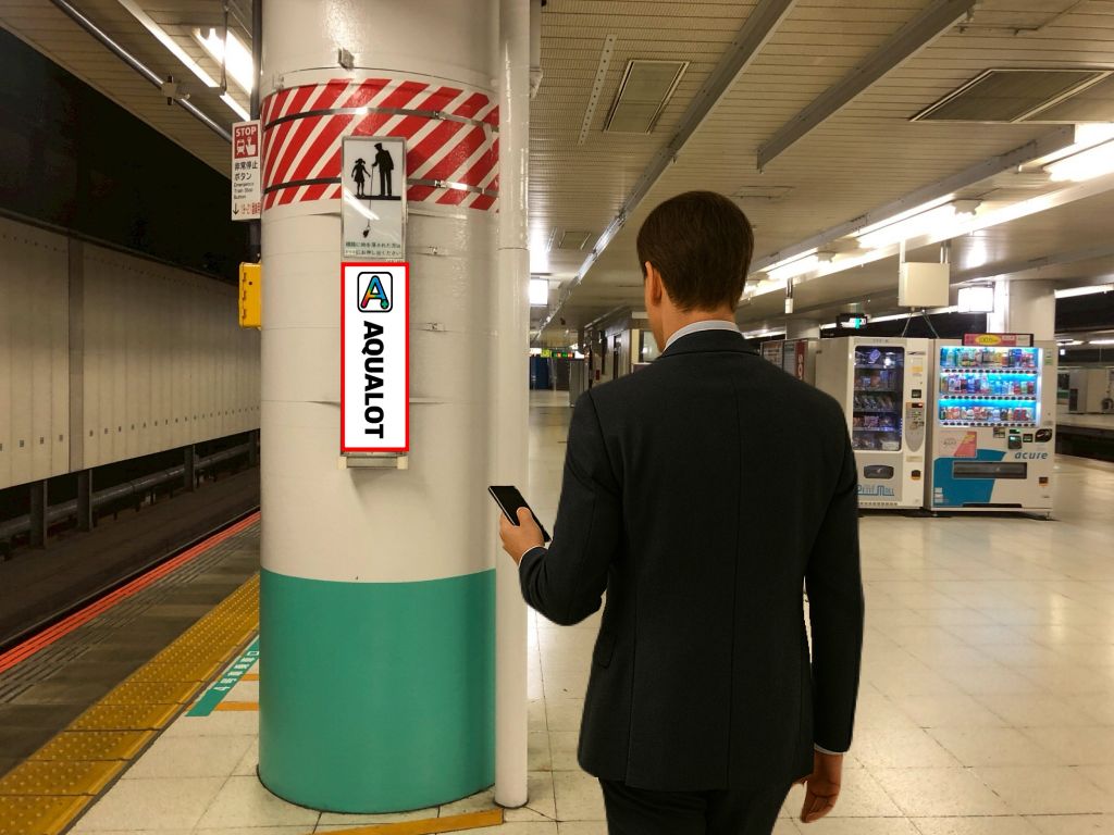 通勤中のビジネスパーソンが駅ホームでAQUALOTの広告を見ている様子