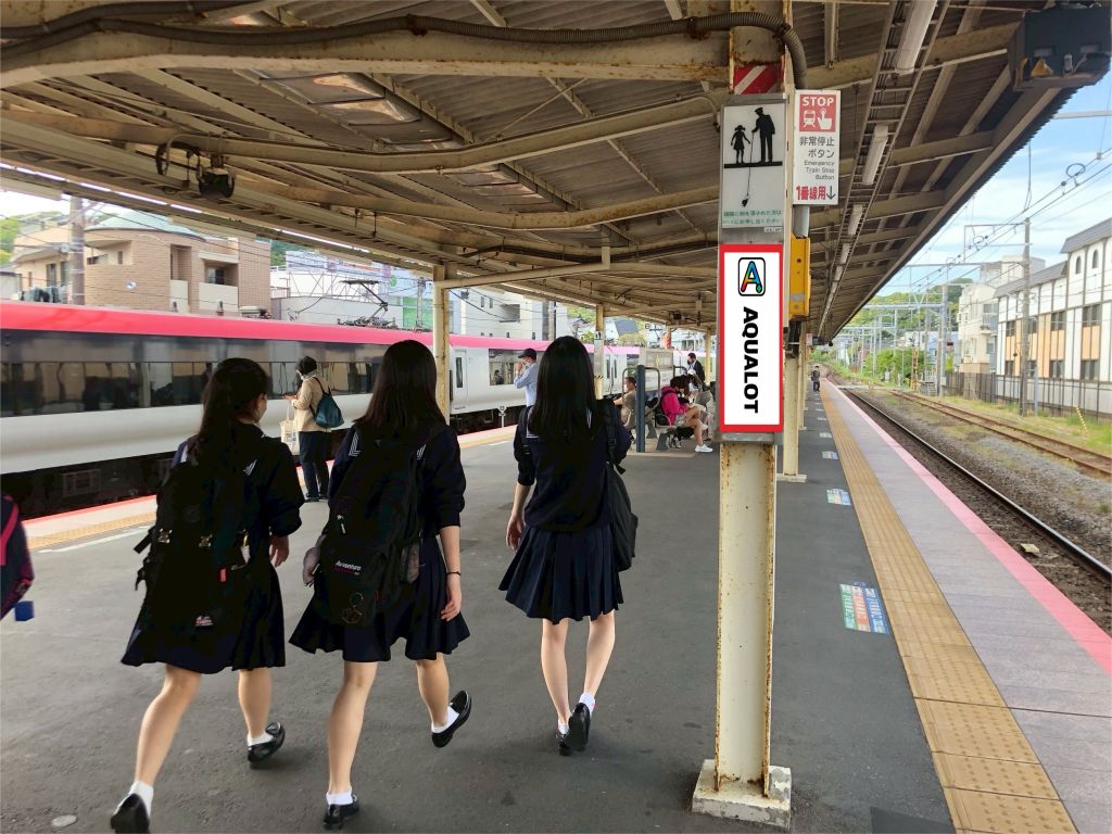 駅で集まる学生グループとAQUALOTの広告